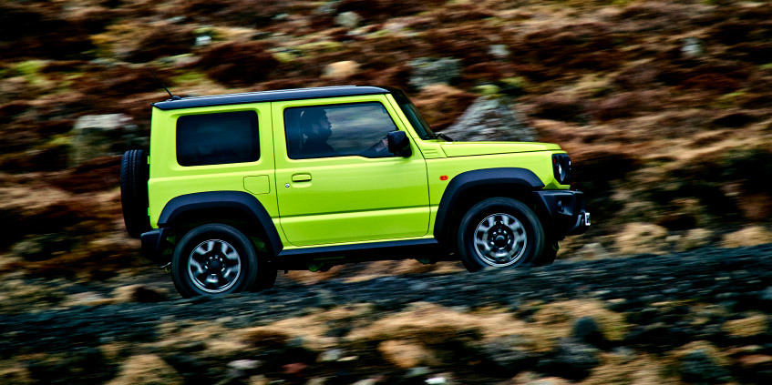 Suzuki Jimny verde neón acelera por un camino de tierra rodeado de vegetación.